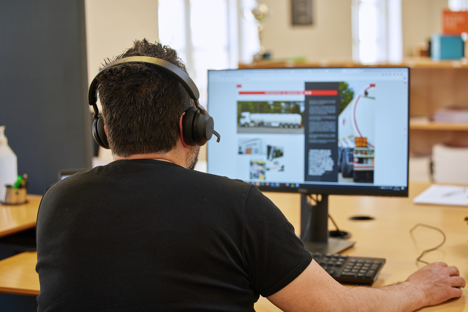 A man sitting at a desk and working while wearing a headset and talking to a customer.